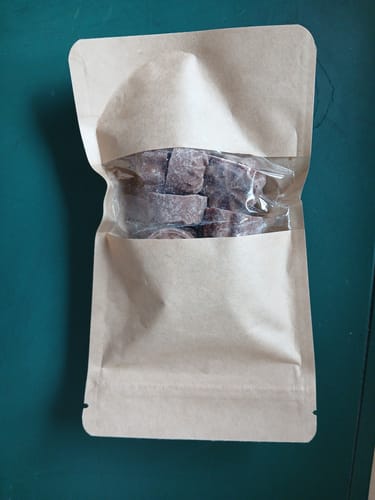 Ein Kunde zeigt den geöffneten Papierbeutel mit den THC Happy Hasch Schoko Flower Stücken darin.