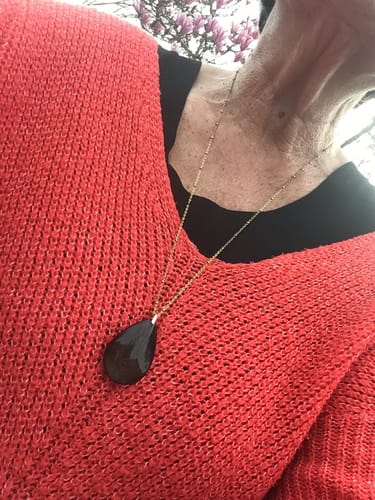 Cliente portant son pendentif Obsidienne Dorée en forme de goutte sur un pull en maille de couleur corail.