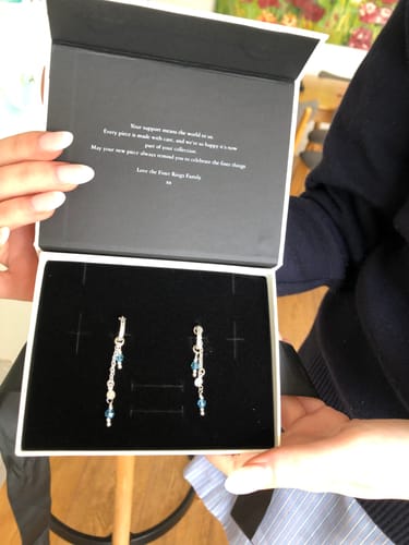 Reviewer holding an open jewelry box displaying the silver Gemma Earrings with custom blue stones.