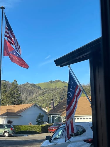 Customer photo showing two American flags, one on a flagpole and another on a car, in a sunny neighborhood.