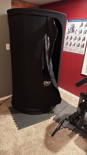Customer's black Sauna Pod 2.0 set up in a home gym with the zippered door partially open.