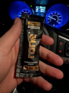 Customer holding a black SuperCharged Honey packet in a car with a glowing dashboard.