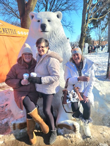 Reviewer and two other people posing happily outdoors with a large polar bear statue.