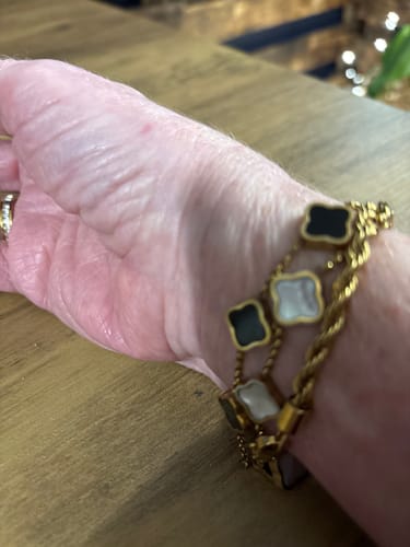 Close-up of a reviewer wearing layered gold-tone bracelets with clover-shaped charms.