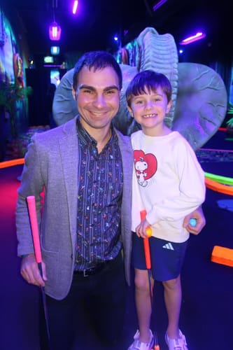 Customer wearing the Mega Man "Mega Pixels" shirt under a gray blazer while playing indoor mini-golf.