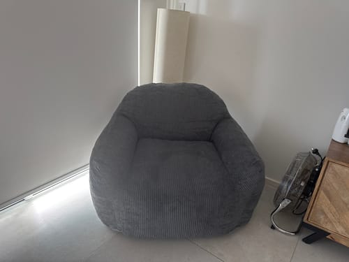 Customer's grey corduroy lounge chair placed in the corner of a room, next to a window.