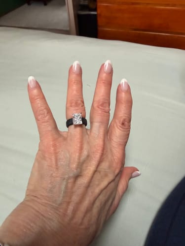 A reviewer's hand wearing the black Silicone Ring, showing the large, sparkling emerald-cut CZ stone.