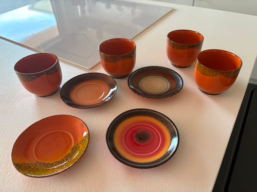 Klant toont de vier HKliving 70's Ceramics schotels met bijpassende oranje kopjes, uitgestald op een wit aanrecht.