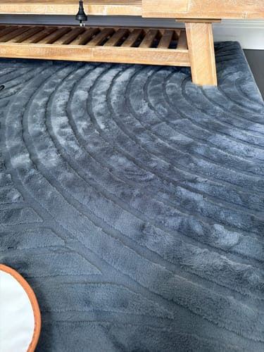 Customer's charcoal grey Relax Mat on a floor, showing its soft, wavy-patterned texture under a wooden furniture leg.