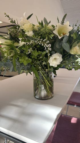Reviewer's lush White Purity Vase Arrangement with white flowers and greenery in a glass vase on a table.