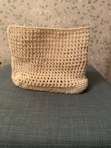 Customer's unfinished CrochetPark™ Haven Hobo bag in cream yarn, sitting upright on a teal cushion.