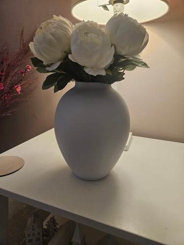 Reviewer's matt white Ella Vase with white peonies, displayed on a white table in a softly lit room.