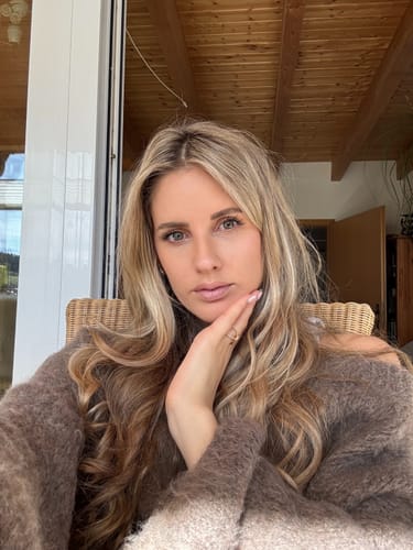 Rezensentin trägt das weiche, braune Ultra-Soft Off-Shoulder Pulloverkleid und sitzt in einem Stuhl.