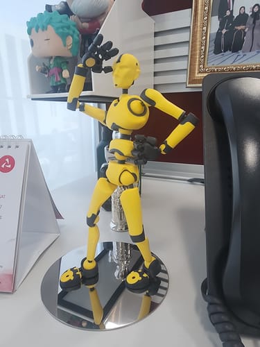 Customer's yellow and black Solar Flare Stickybones figure in a dynamic pose on its reflective stand on an office desk.