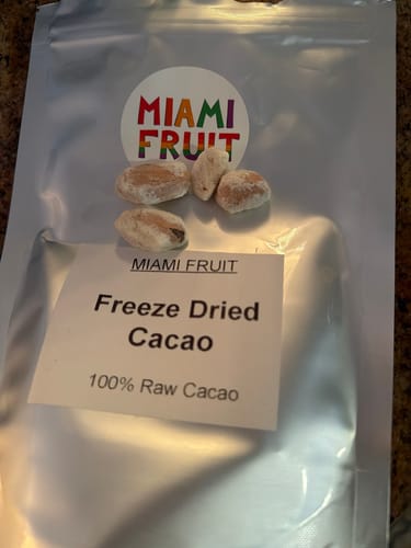 Customer's silver pouch of Freeze Dried Cacao with four light-colored cacao beans on display.