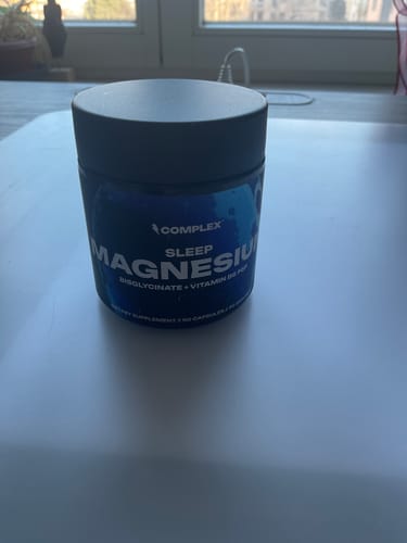 Customer's dark blue tub of Sleep Magnesium supplement sitting on a white table.