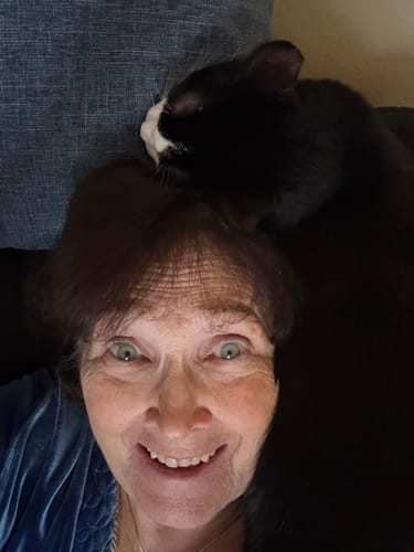 A happy reviewer's close-up selfie showing their facial skin, with a cat snuggling on their head.