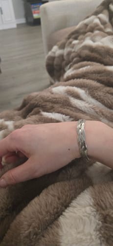 Customer's wrist wearing the silver-toned, braided Palm Beach Bracelet while resting on a plush blanket.