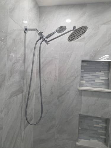 Customer's modern, all-metal handheld shower head installed as part of a dual system in a tiled shower.