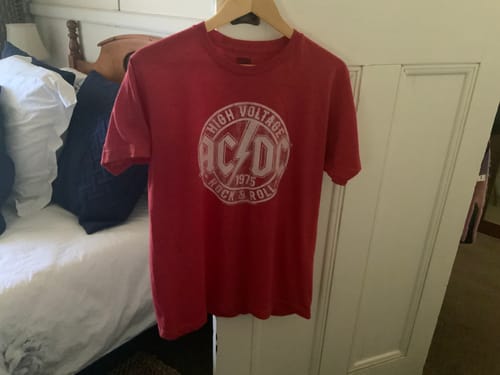 Reviewer's red High Voltage Rock and Roll ACDC T-Shirt hanging on a wooden hanger.