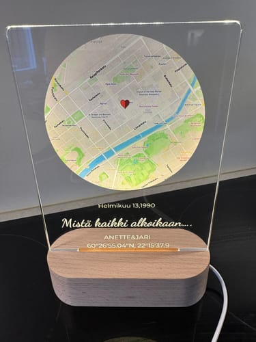 Ein Kunde zeigt das personalisierte Nachtlicht „Wo alles begann“ mit beleuchteter Karte und Holzsockel.