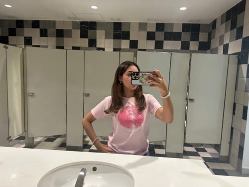 Reviewer taking a mirror selfie in a bathroom wearing the pink Studio 54 baby tee.