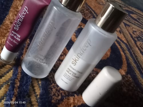 Reviewer's used and new bottles of Dream Glaze Peptide Milk Toner on a textured surface.