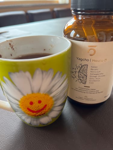 Rezensent zeigt das Yagcho Neuro C Produkt neben einer Tasse mit dem zubereiteten Getränk