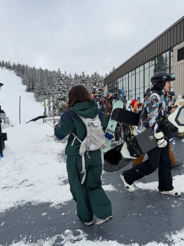 Reviewer from behind wearing the dark green baggy snow pants at a snowy resort.