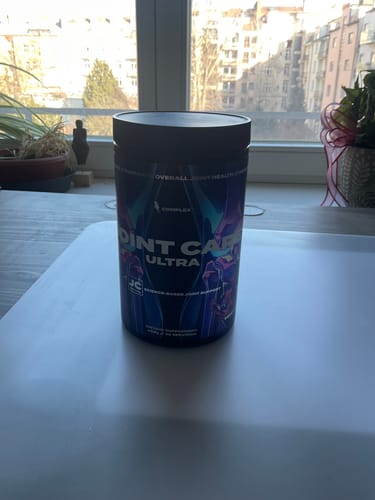 Customer's black tub of Joint Care Ultra supplement on a white table in front of a window.