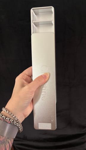 Reviewer holding the silver metal Weekly Case with the lid partially open, showing the empty compartments and textured grip.