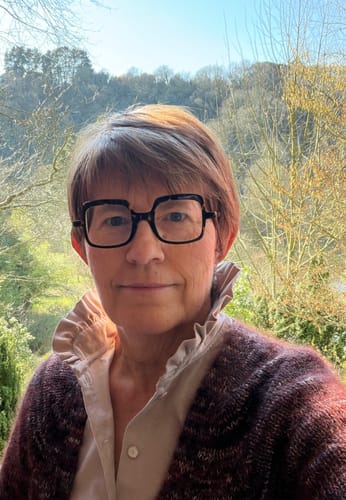 Cliente portant la Blouse Marthe en velours sable avec son col à froufrous visible sous un gilet.