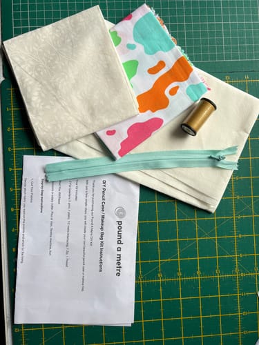 Customer's free DIY bag bundle, showing two fat quarters, interfacing, a zipper, thread, and instructions on a cutting mat.