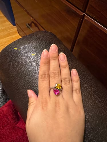 Customer's hand wearing the Navae Birthstone Ring with a yellow radiant-cut and a pink pear-cut stone.
