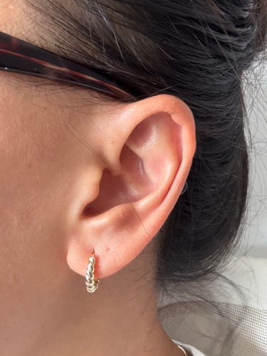 Reviewer's ear in a close-up, wearing the small, gold Mini Croissant Huggie Earring.