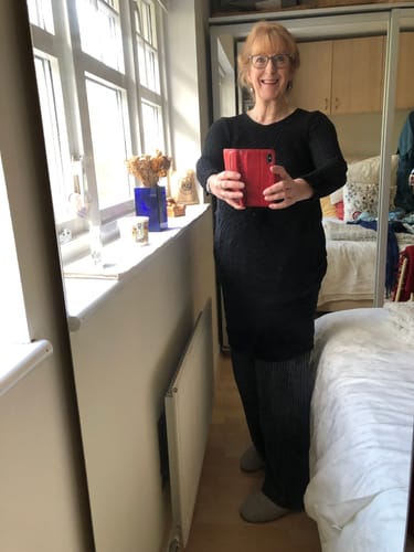 Customer wearing the black crinkled silk midi dress over trousers in a bedroom setting.