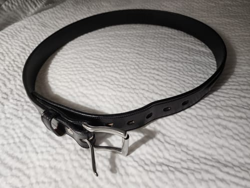 Customer's black Esquire Raised belt coiled on a bed, showing the raised center and silver buckle.