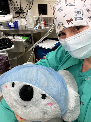 Reviewer in scrubs wearing a patterned DuoStyle Scrub Hat, holding a stuffed koala that is also wearing a surgical cap.