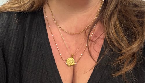 Close-up of a reviewer wearing the Coral Necklace layered with two other gold necklaces.