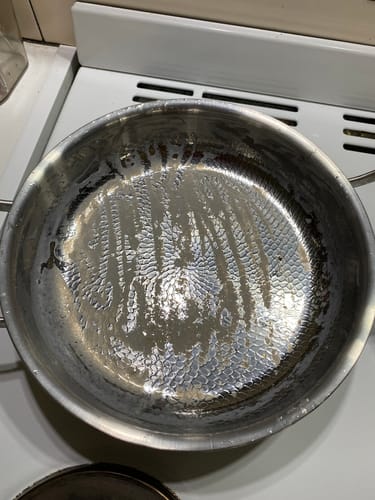 Rezensent zeigt die nasse, gehämmerte Titanpfanne auf einem Herd.