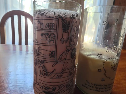 Cliente muestra el vaso Cat Lover lleno de líquido rosa junto a otro vaso en una mesa.