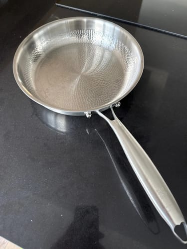 Ein Kunde zeigt die gehämmerte Titanpfanne, die auf einer sauberen, schwarzen Herdplatte steht.