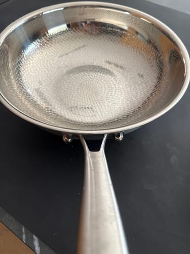 Rezensent zeigt eine Nahaufnahme der leeren, gehämmerten Titanpfanne auf einem Kochfeld.