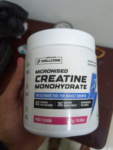 Customer holding a white tub of Wellcore Micronised Creatine Monohydrate in Fruit Fusion flavor.