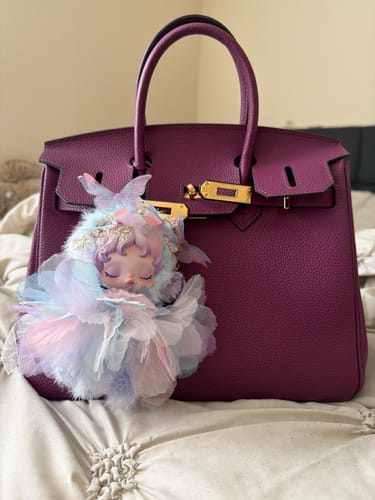 Customer's magenta leather Warkin Bag with gold hardware, displayed on a bed with a cute fairy charm attached.