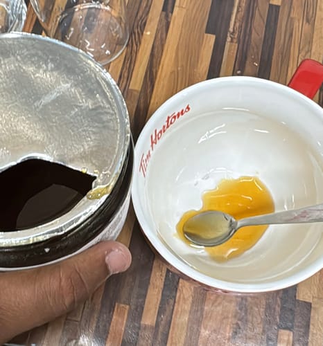 Close-up of a reviewer scooping dark Raw Forest Honey from the open jar into a mug.