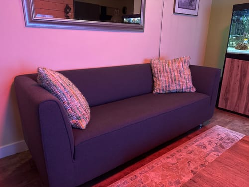 Klant toont twee veelkleurige Sierkussen Verano kussens op een donkere bank in een woonkamer.