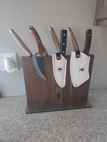 Reviewer's walnut magnetic knife holder on a counter, holding several different knives, some with sheaths.