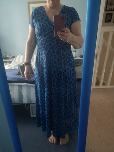 Kundin steht vor einem Spiegel und trägt das bodenlange, blaue Kleid mit Leopardenmuster und V-Ausschnitt.