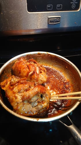 Rezensent brät Hähnchen in einer dunklen Soße in der gehämmerten Titanpfanne.